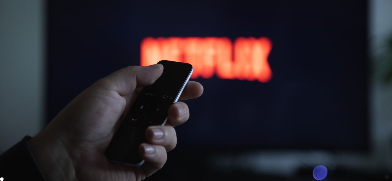 A hand holding a remote in front of a TV screen in a dark room.