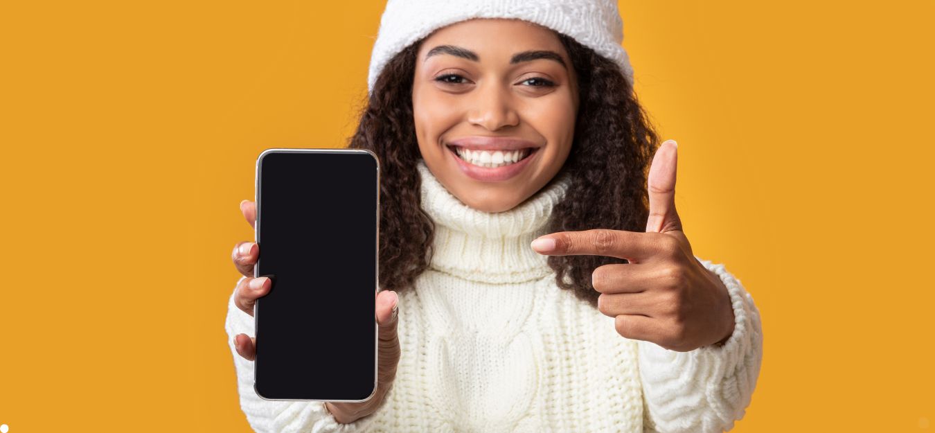 A woman holding a cell phone. She is standing in front of a yellow wall.