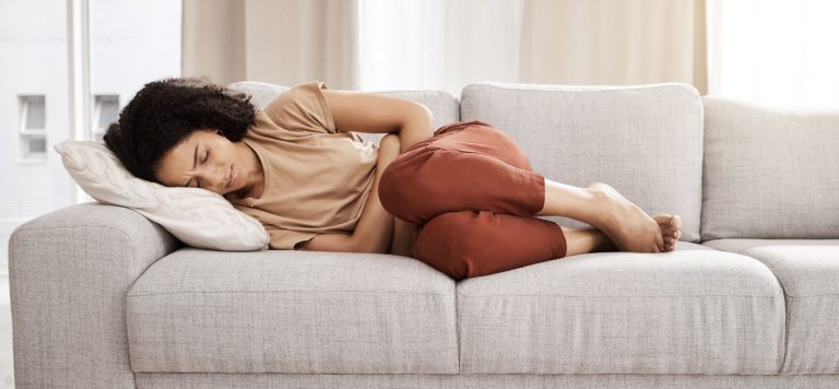 A woman laying on a grey couch, holding her stomach.