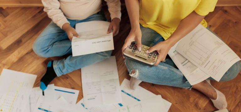 A couple sitting on the floor. They are surrounded by paper bills all over the floor.