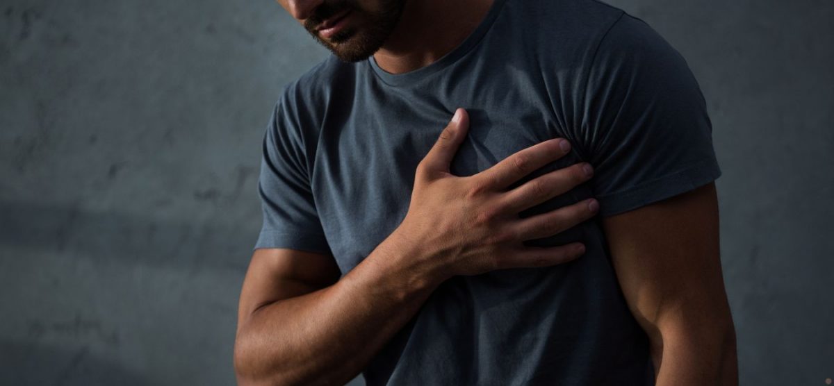 A man in a blue tshirt holding his hand to his chest, as if experiencing chest pain.