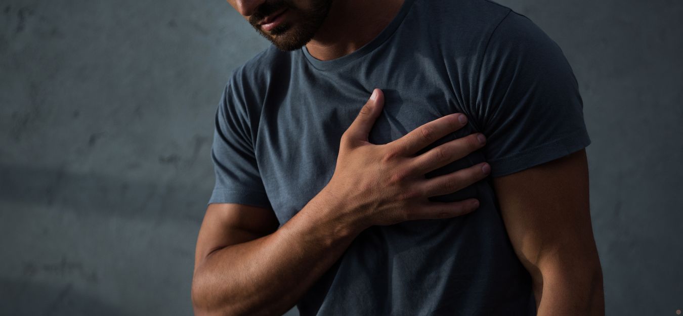 A man in a blue tshirt holding his hand to his chest, as if experiencing chest pain.