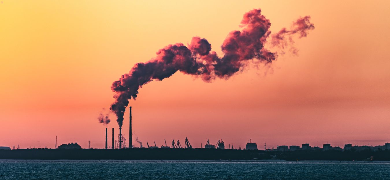 A factory releasing air pollution against an orange sky.