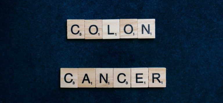 The words "colon cancer" spelled out in Scrabble tiles on a dark background.