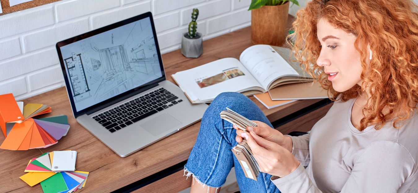 A woman sitting in front of a laptop, looking at color swatches.