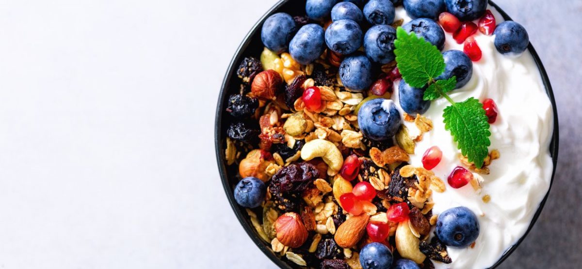 A bowl of yogurt with granola and blueberries on top.