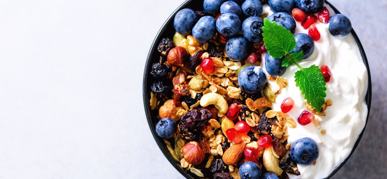 A bowl of yogurt with granola and blueberries on top.