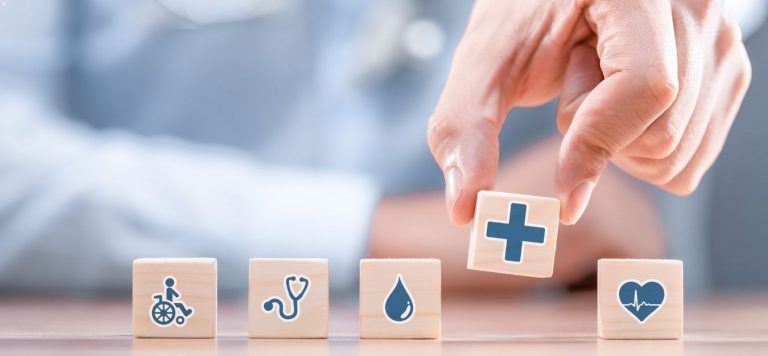 A hand lining up small wooden cubes. The cubes have blue healthcare icons on them